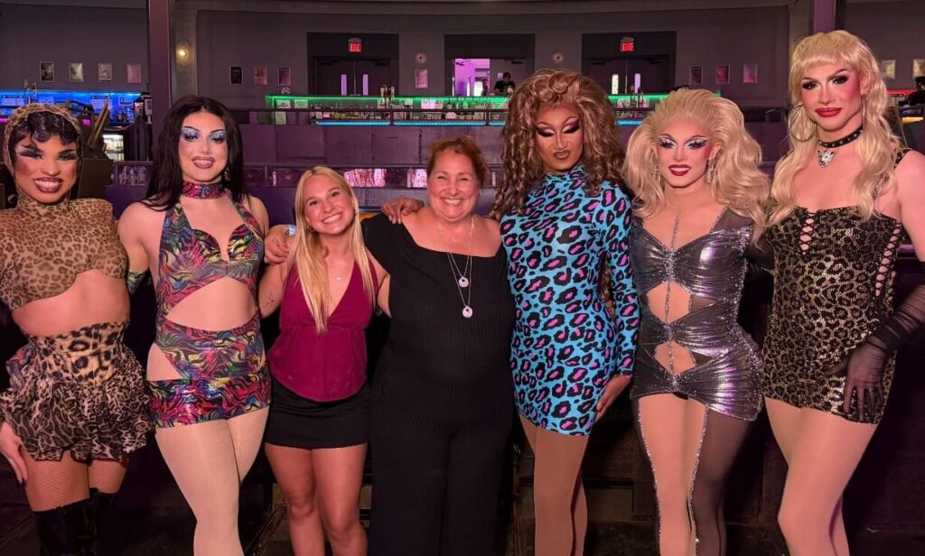 Group photo of community members and performers gathered at an LGBTQ+ community event, celebrating inclusion, connection, and support in a welcoming social setting.