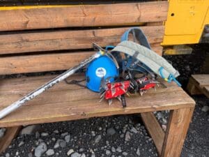 Ice climbing equipment in Iceland, including a blue helmet, ice axe, crampons, and backpack arranged on a wooden bench.